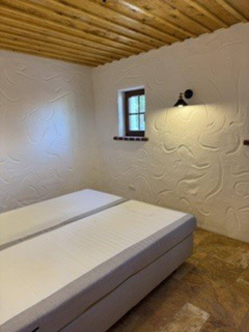 Schlafzimmer mit Holzbalkendecke, strukturierten Wänden und zwei Einzelbetten.