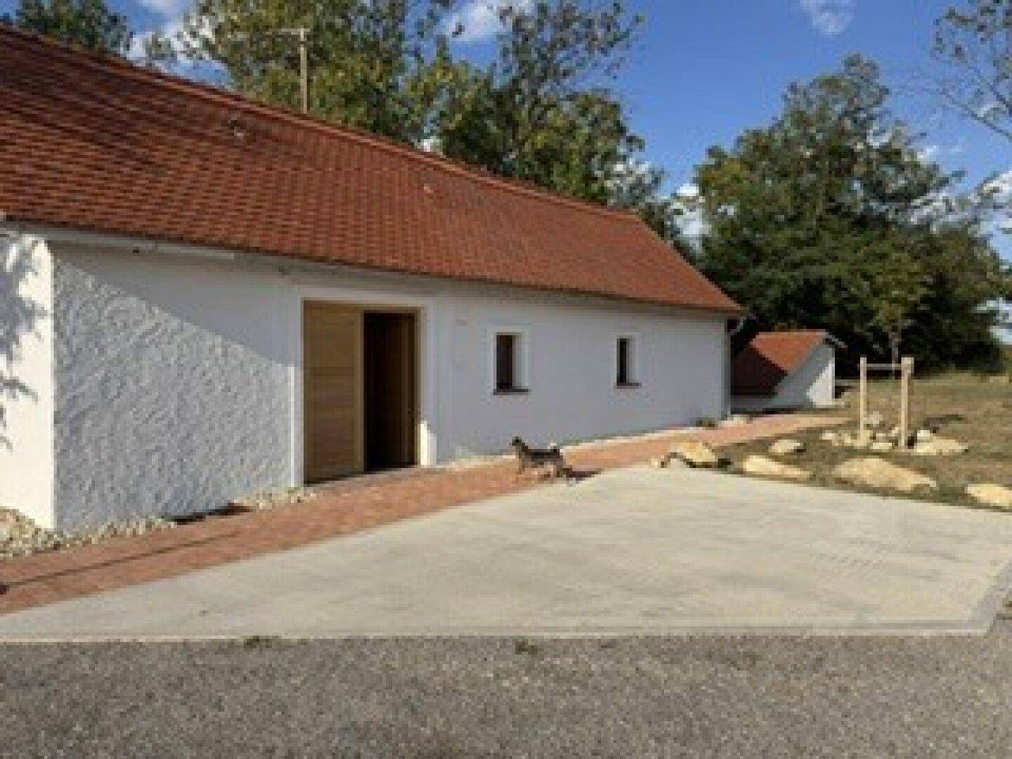 Weiß verputztes Gebäude mit rotem Ziegeldach und einem kleinen Hund vor dem Eingangsbereich.