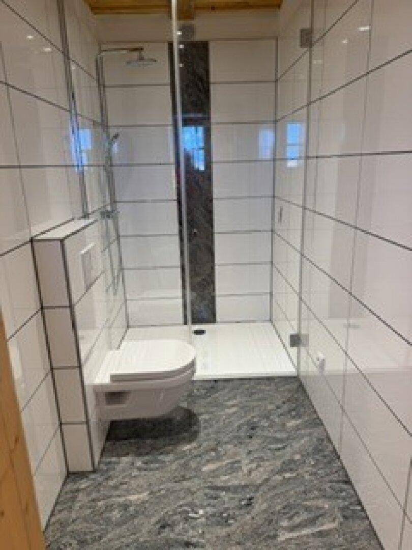 Modernes Badezimmer mit weißen Fliesen, begehbarer Dusche und wandhängendem WC.