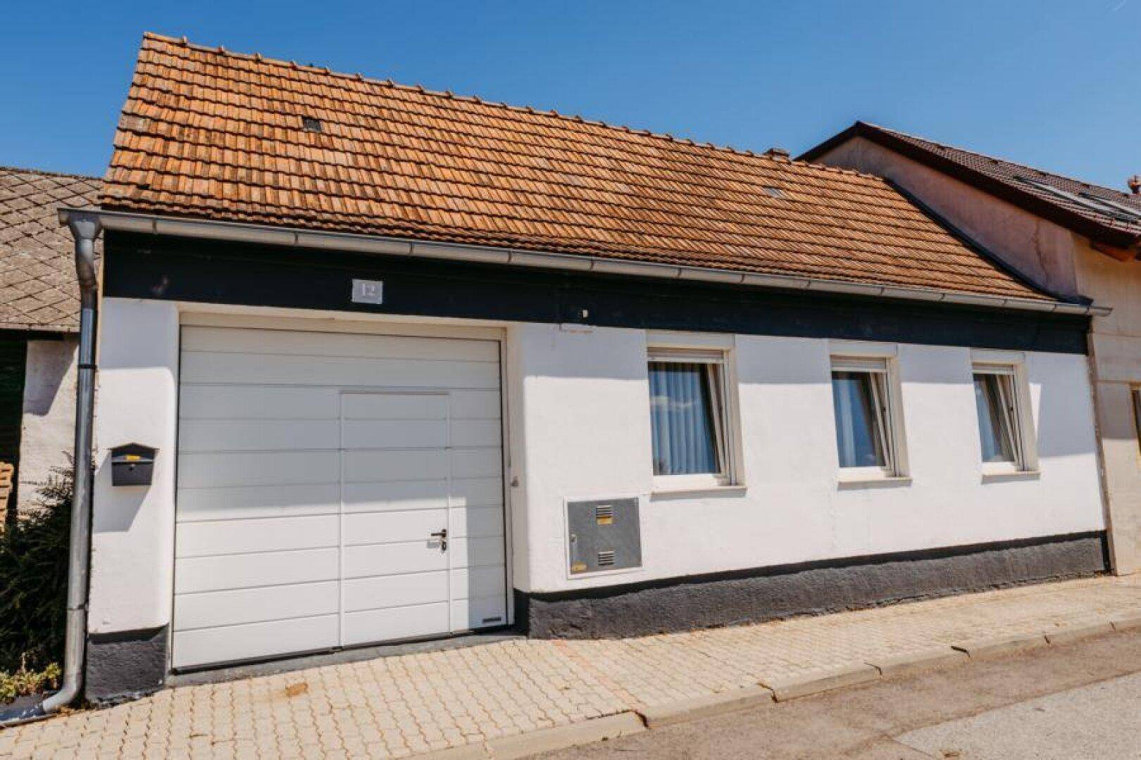 Seitenansicht des Hauses mit weißer Fassade, Garagentor und traditionellem Ziegeldach.