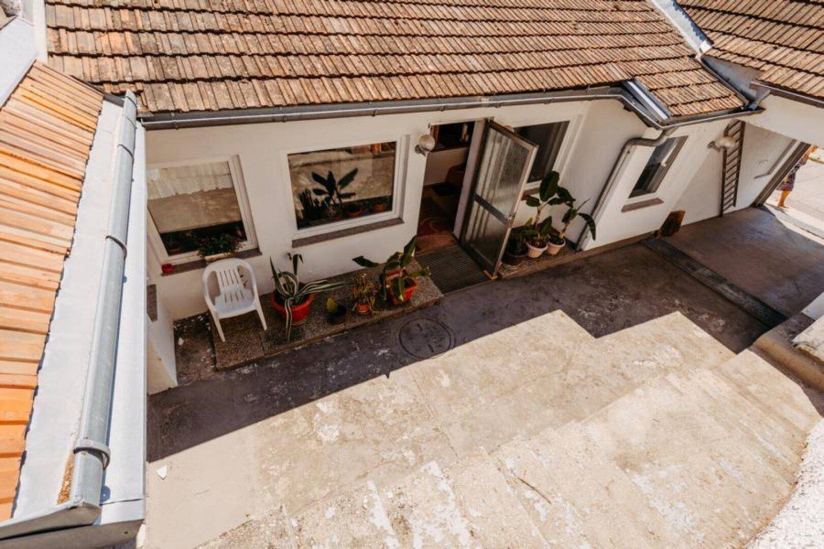 Blick von oben auf einen gepflasterten Innenhof mit Topfpflanzen und Zugang zum Haus.