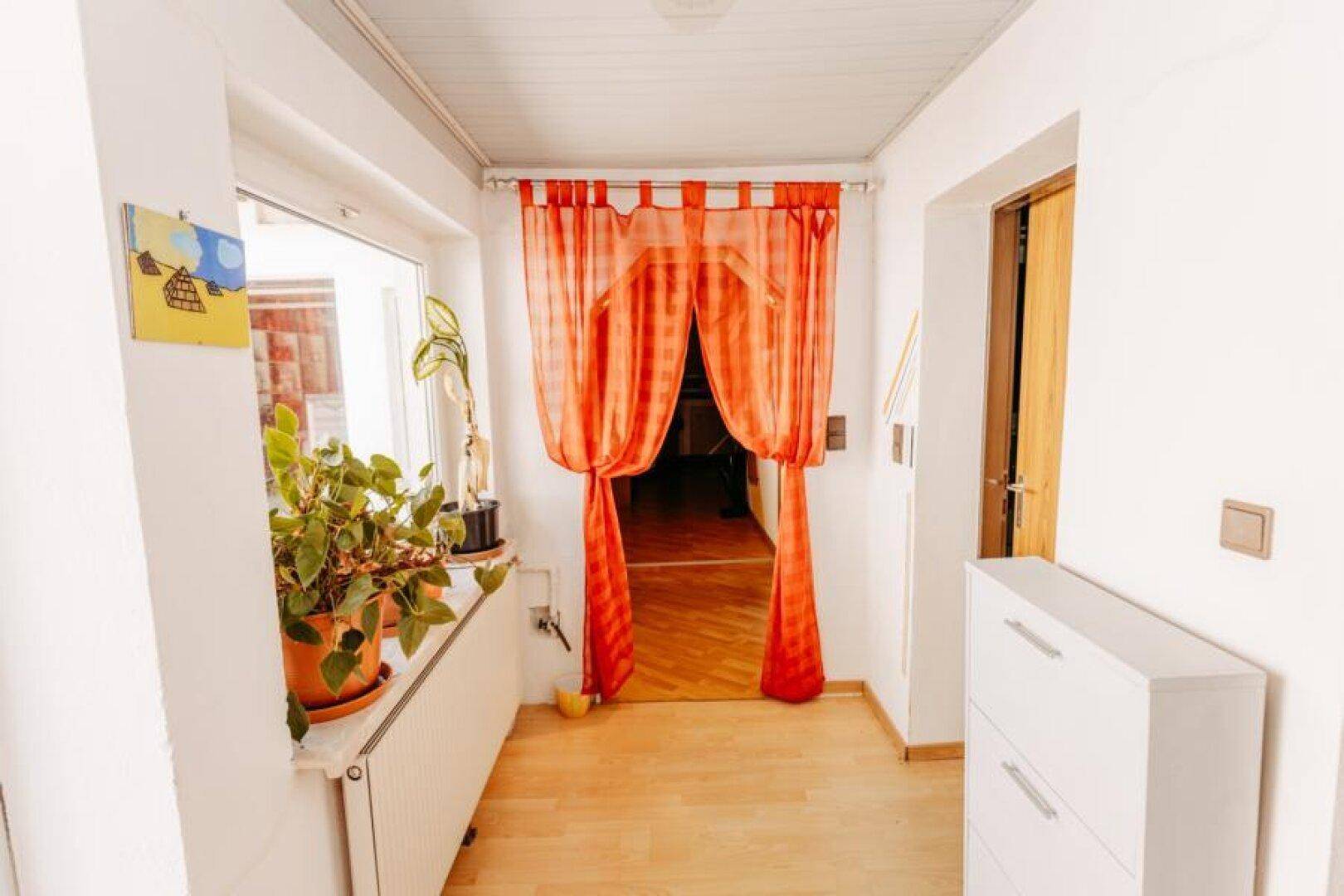 Flur mit hellem Holzfußboden, Fenster und auffälligen orangefarbenen Vorhängen.