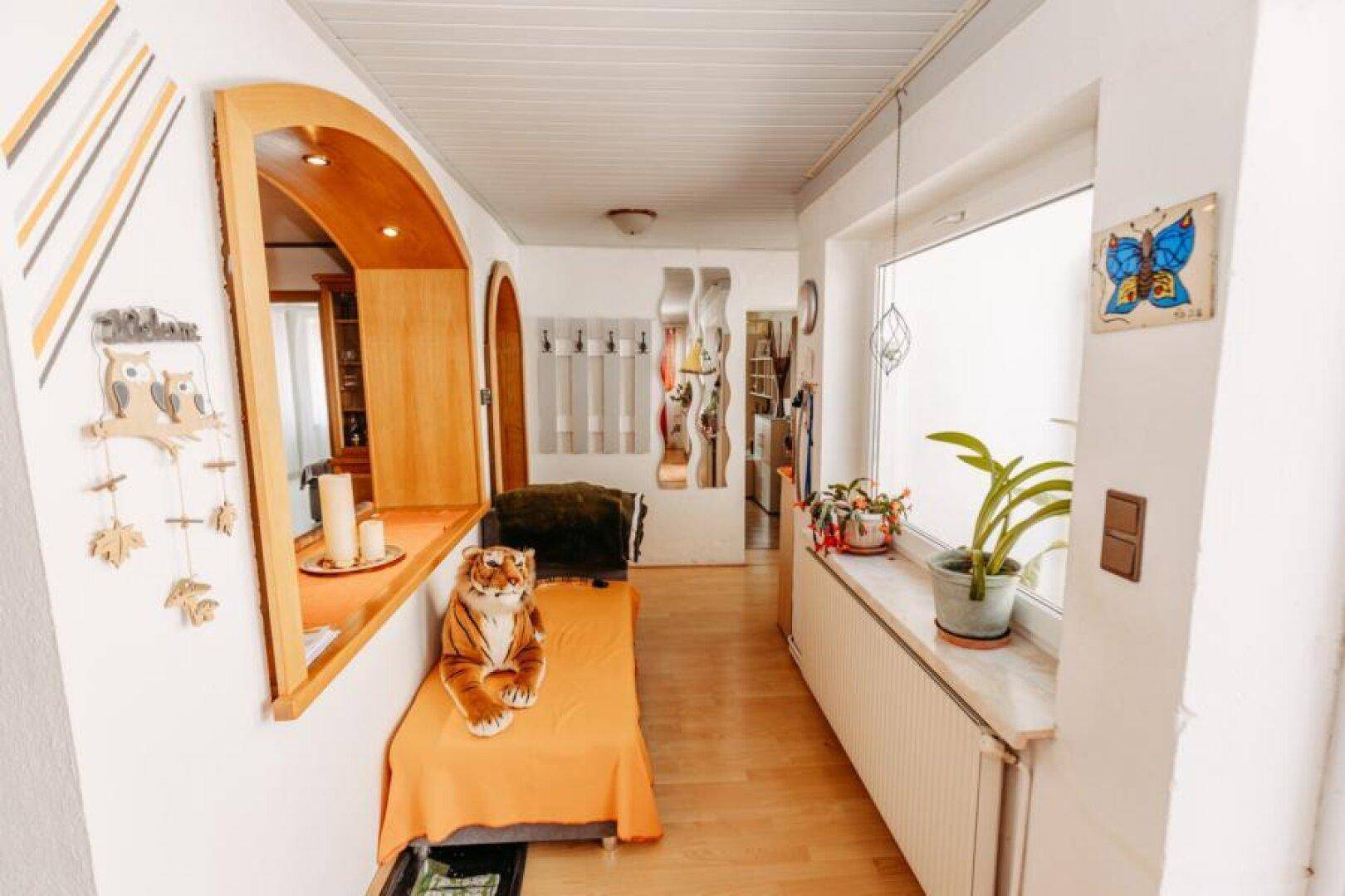 Heller Flur mit Holzfußboden, Fenster und dekorativen Elementen, die zum Wohnbereich führen.