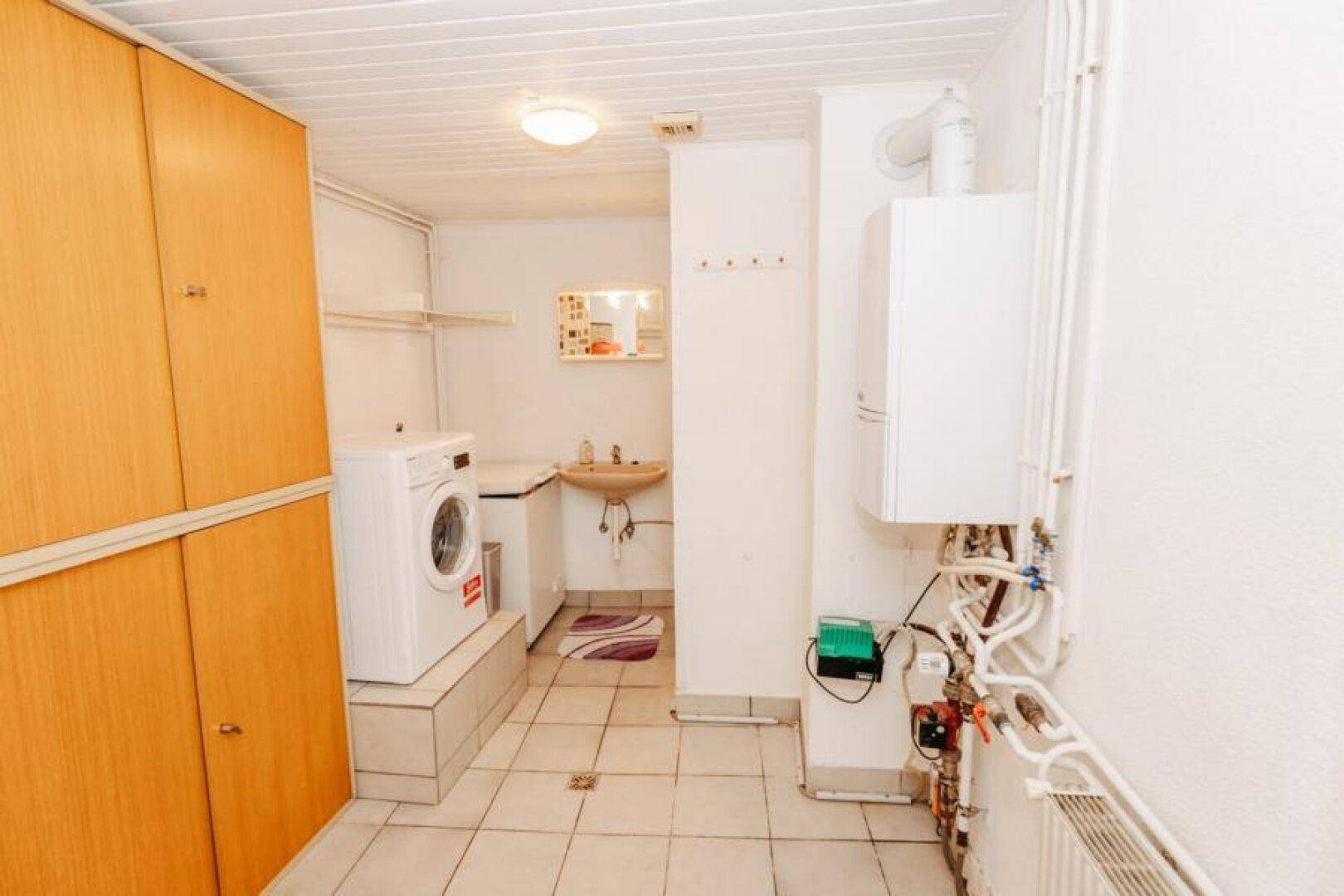 Hauswirtschaftsraum mit Waschmaschine, Spülbecken und sichtbaren Heizungsinstallationen.