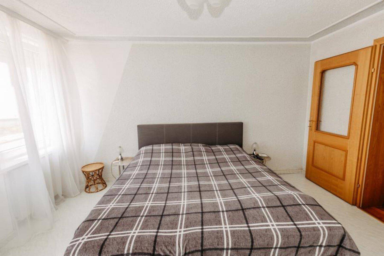 Helles Schlafzimmer mit Doppelbett, schlichten Wänden und einem Fenster mit transparenten Vorhängen.