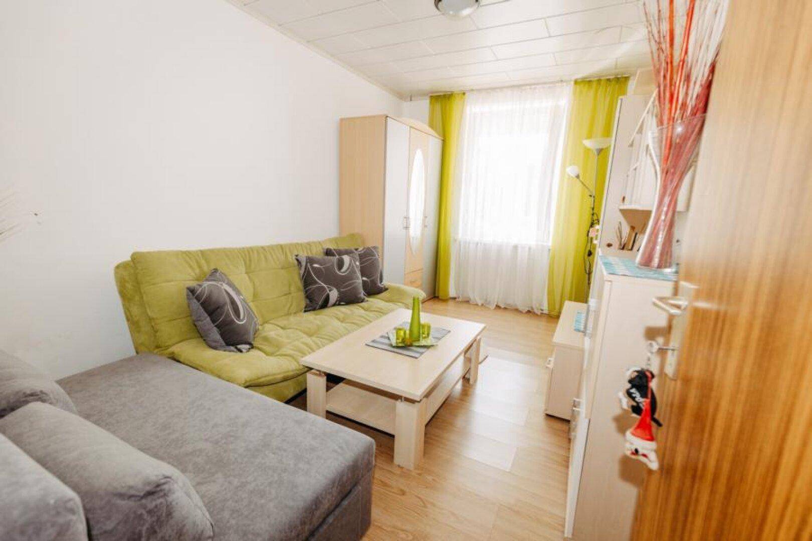 Gemütliches Wohnzimmer mit grünem Sofa, Couchtisch und hellen Holzmöbeln.