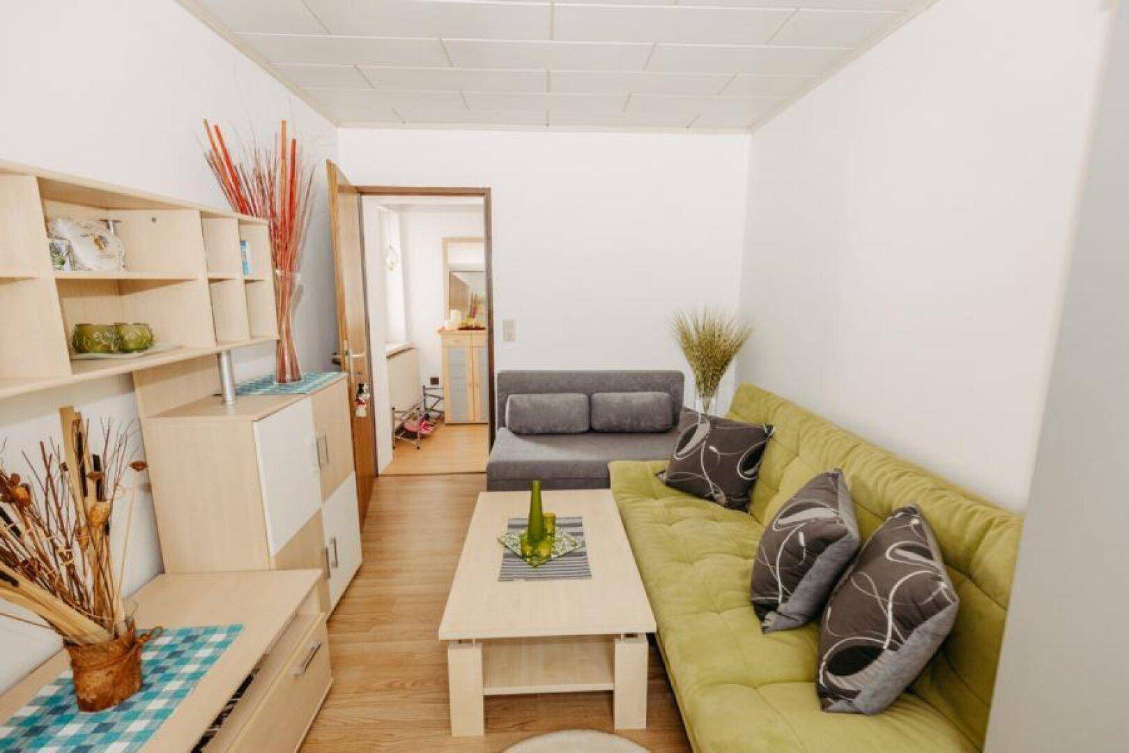 Helles Wohnzimmer mit grünem Sofa, Couchtisch und dekorativen Elementen.