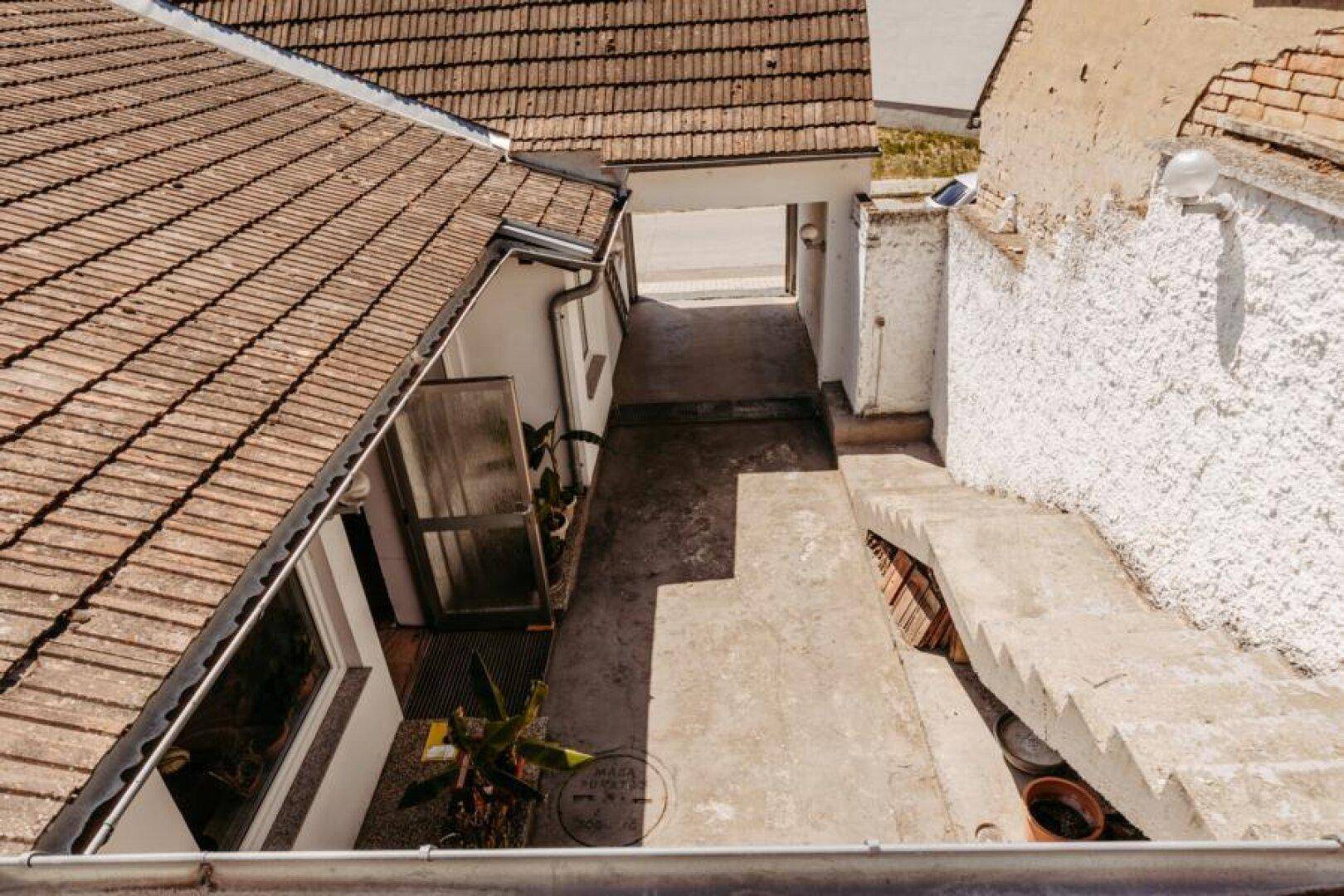 Schmaler Durchgang zwischen Gebäuden mit Steintreppe und Blick auf die traditionellen Dächer.