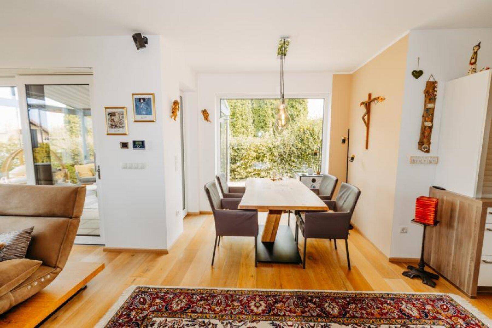 Heller Essbereich mit Holzboden, großem Esstisch und Blick durch das Fenster in den Garten.
