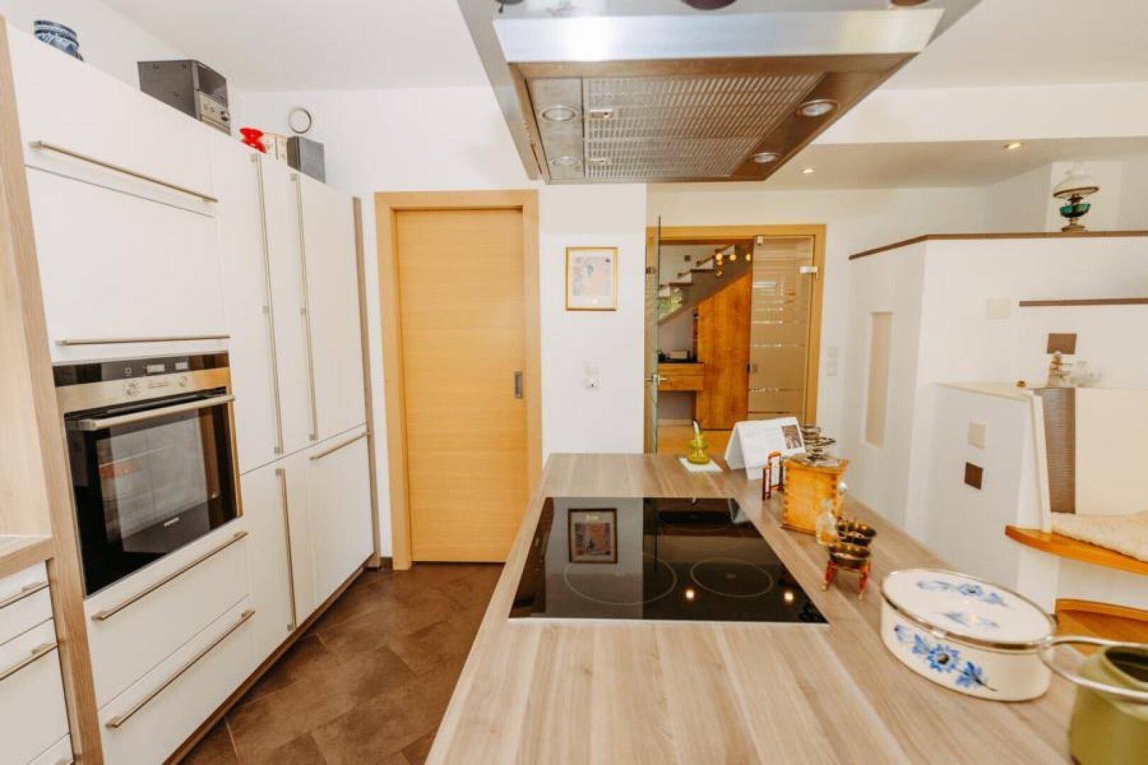 Detailansicht der modernen Küche mit Induktionskochfeld, Backofen und Holztüren im Hintergrund.