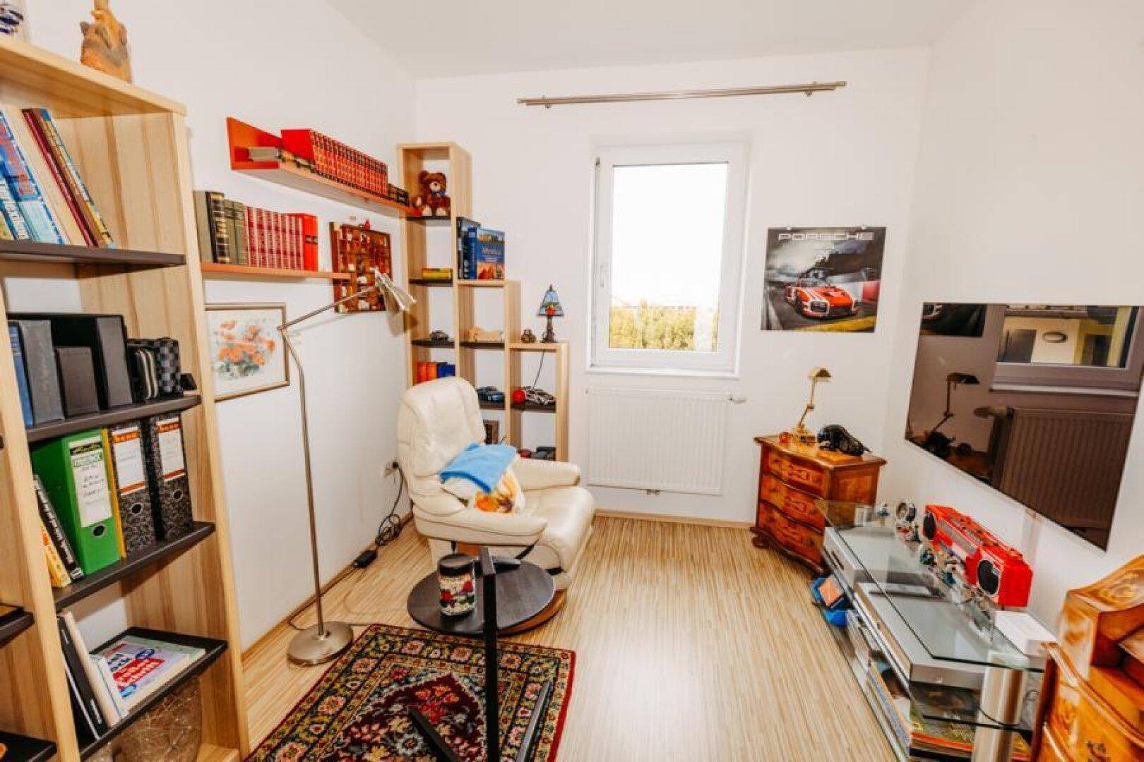 Helles Arbeitszimmer mit Bücherregalen, Schreibtisch und einem bequemen Sessel am Fenster.