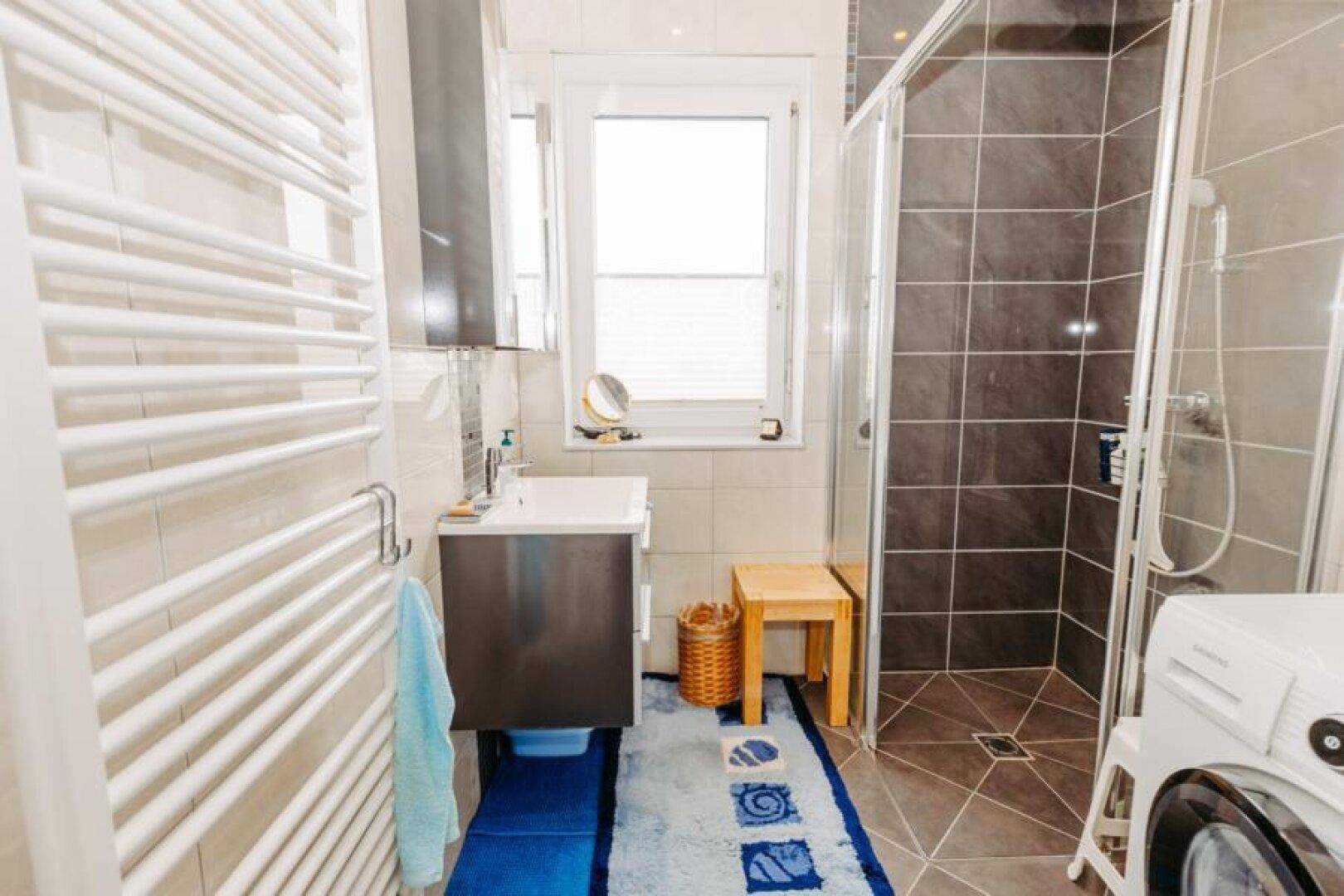 Modernes Badezimmer mit Dusche, Waschbecken, beheiztem Handtuchhalter und Waschmaschine.