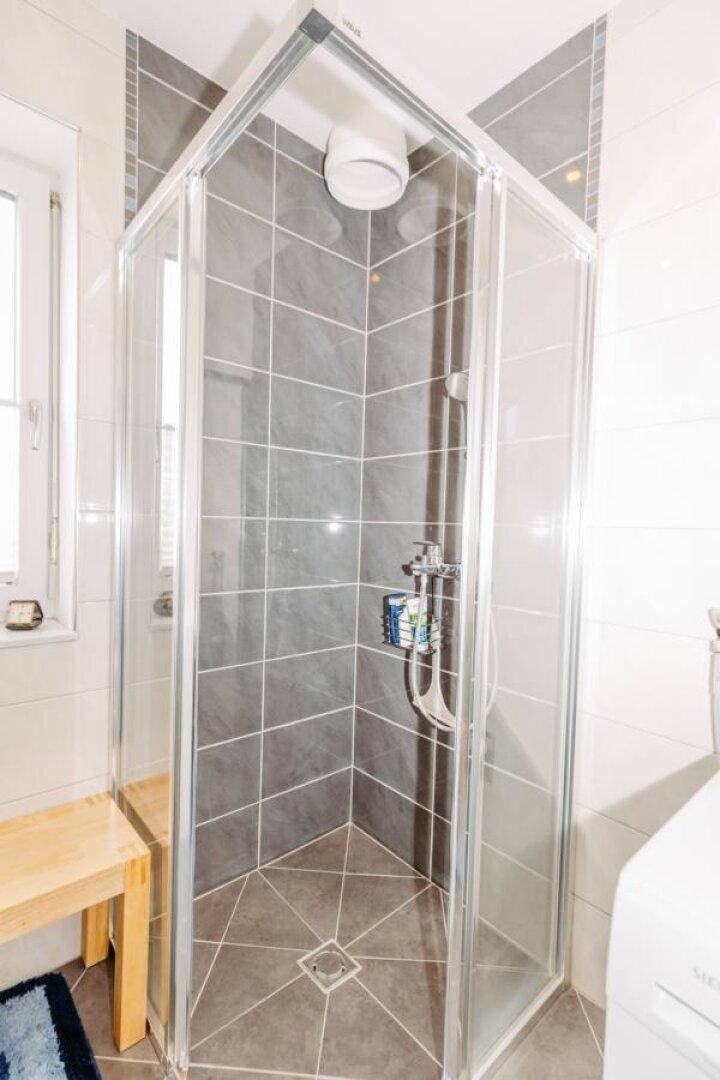 Eckdusche im Badezimmer mit Glaswänden und modernen grauen Fliesen, gut beleuchtet.