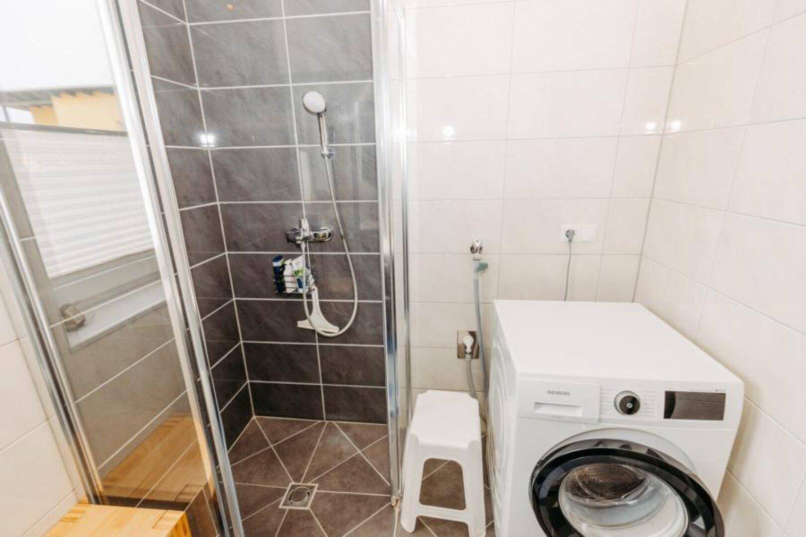 Duschbereich im Badezimmer mit dunklen Fliesen, Glasabtrennung und einer modernen Waschmaschine.