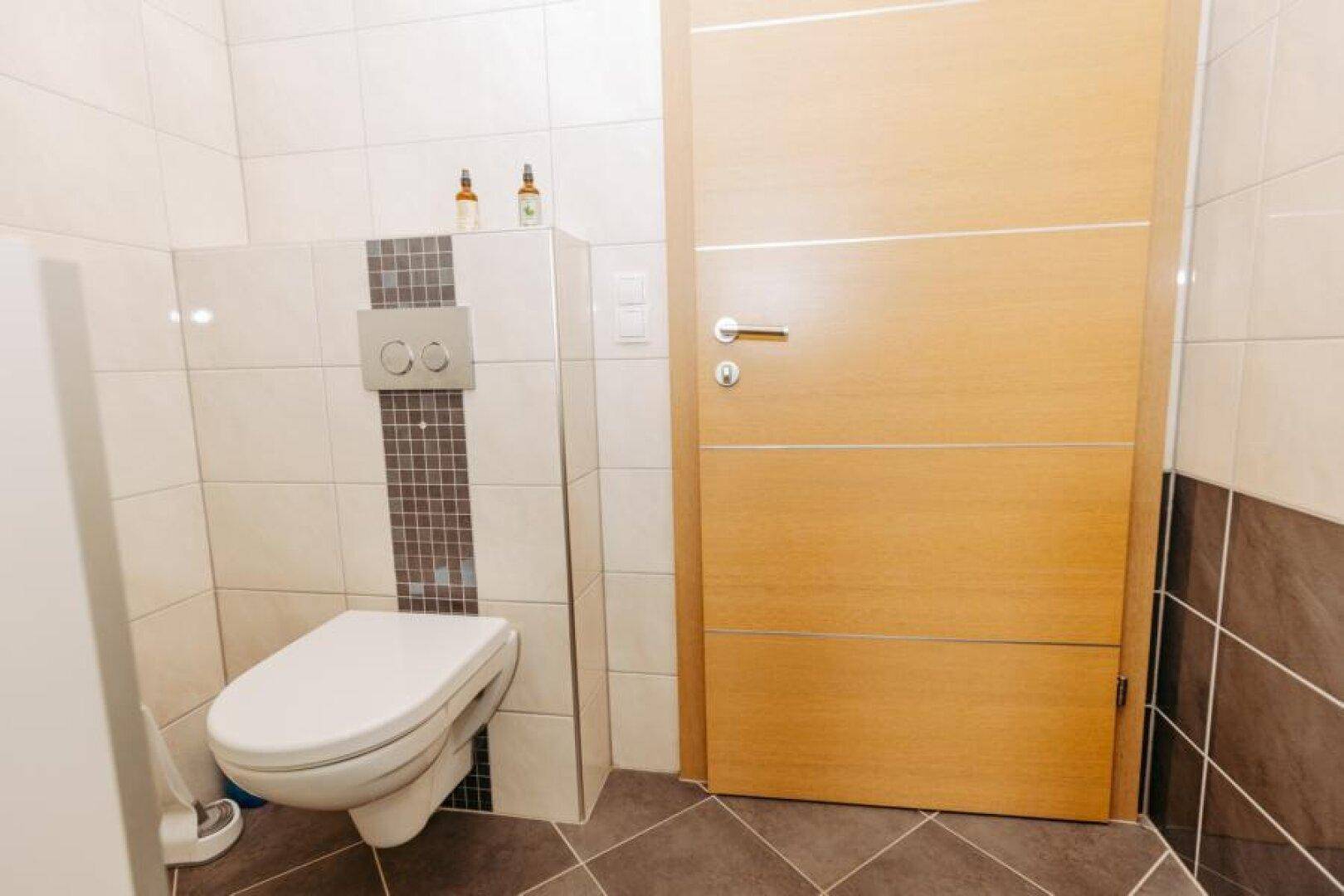 Separate Toilette mit Wand-WC und modernen Fliesen, neben einer Holztür gelegen.