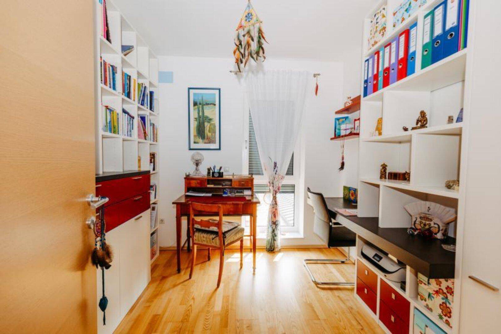 Helles Arbeitszimmer mit vielen Bücherregalen, Schreibtisch und Fenster für natürliches Licht.
