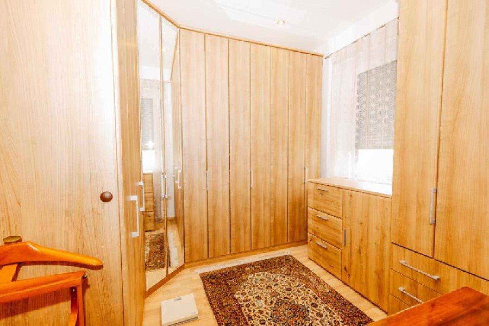 Ankleidezimmer mit vielen Holzschränken, Spiegeltüren und einem Teppich auf dem Boden.