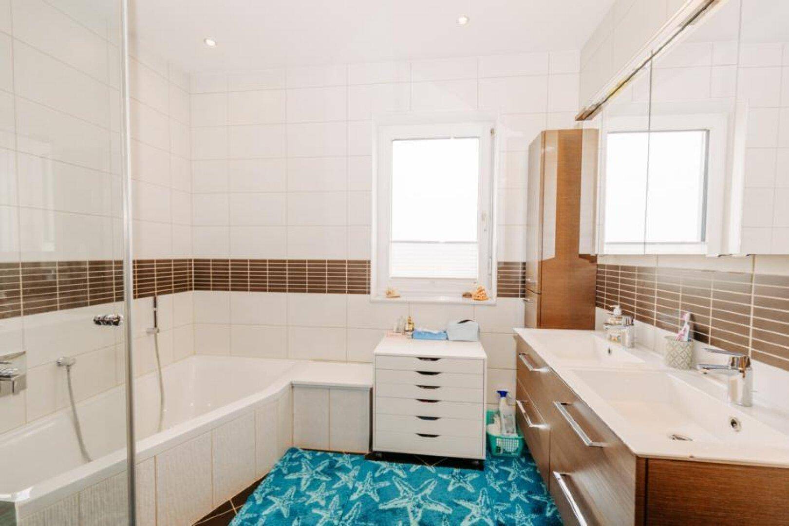 Helles Badezimmer mit Badewanne, Dusche, Doppelwaschbecken und Fenster für natürliche Belüftung.
