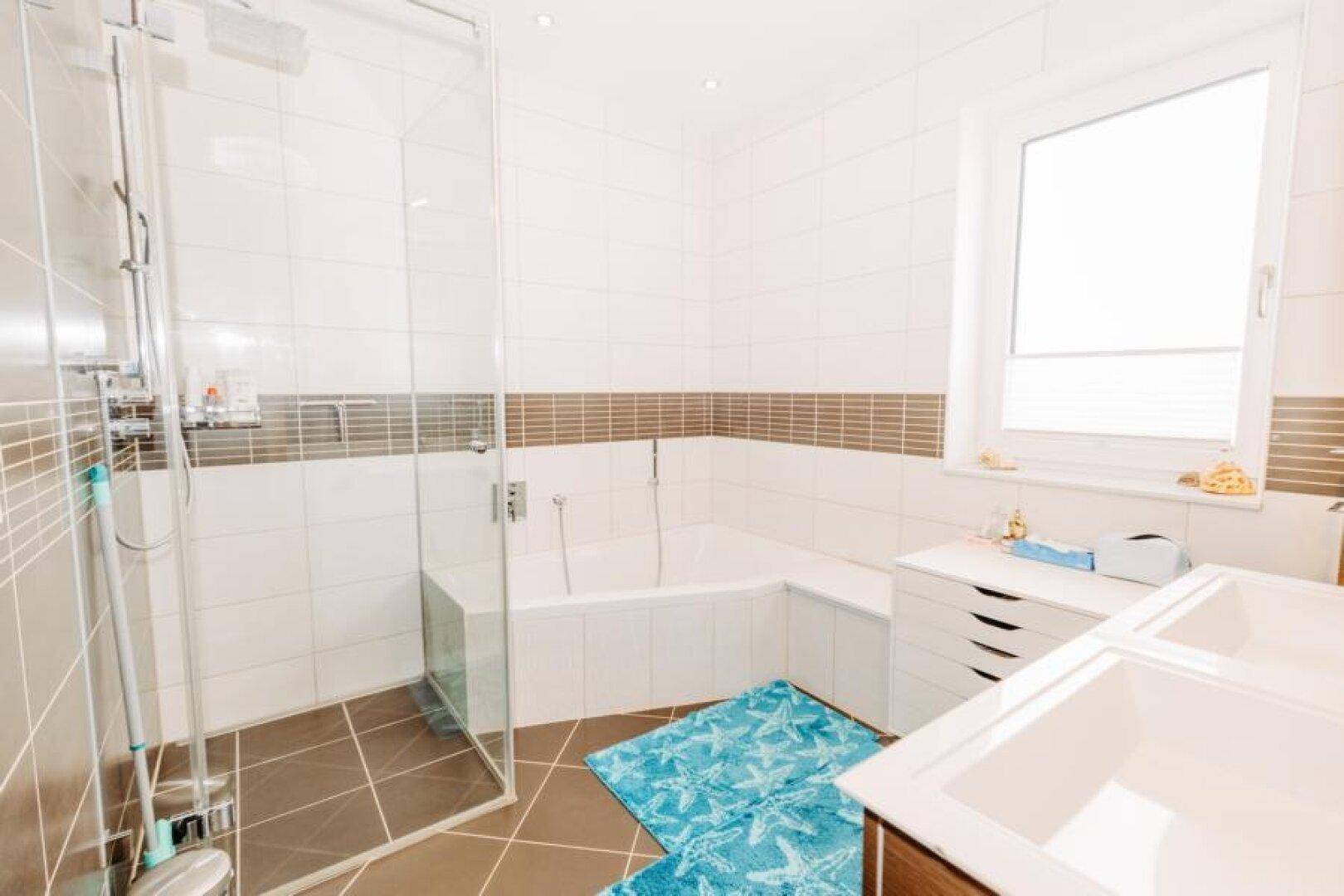 Modernes Badezimmer mit Eckbadewanne, Duschkabine und großem Fenster für viel Tageslicht.