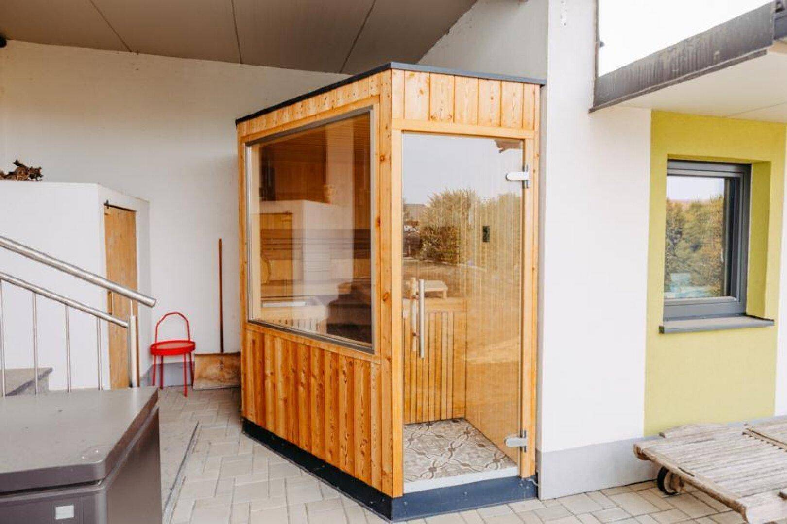 Externe Sauna mit Glasfront neben dem Haus auf einem gepflasterten Bereich.