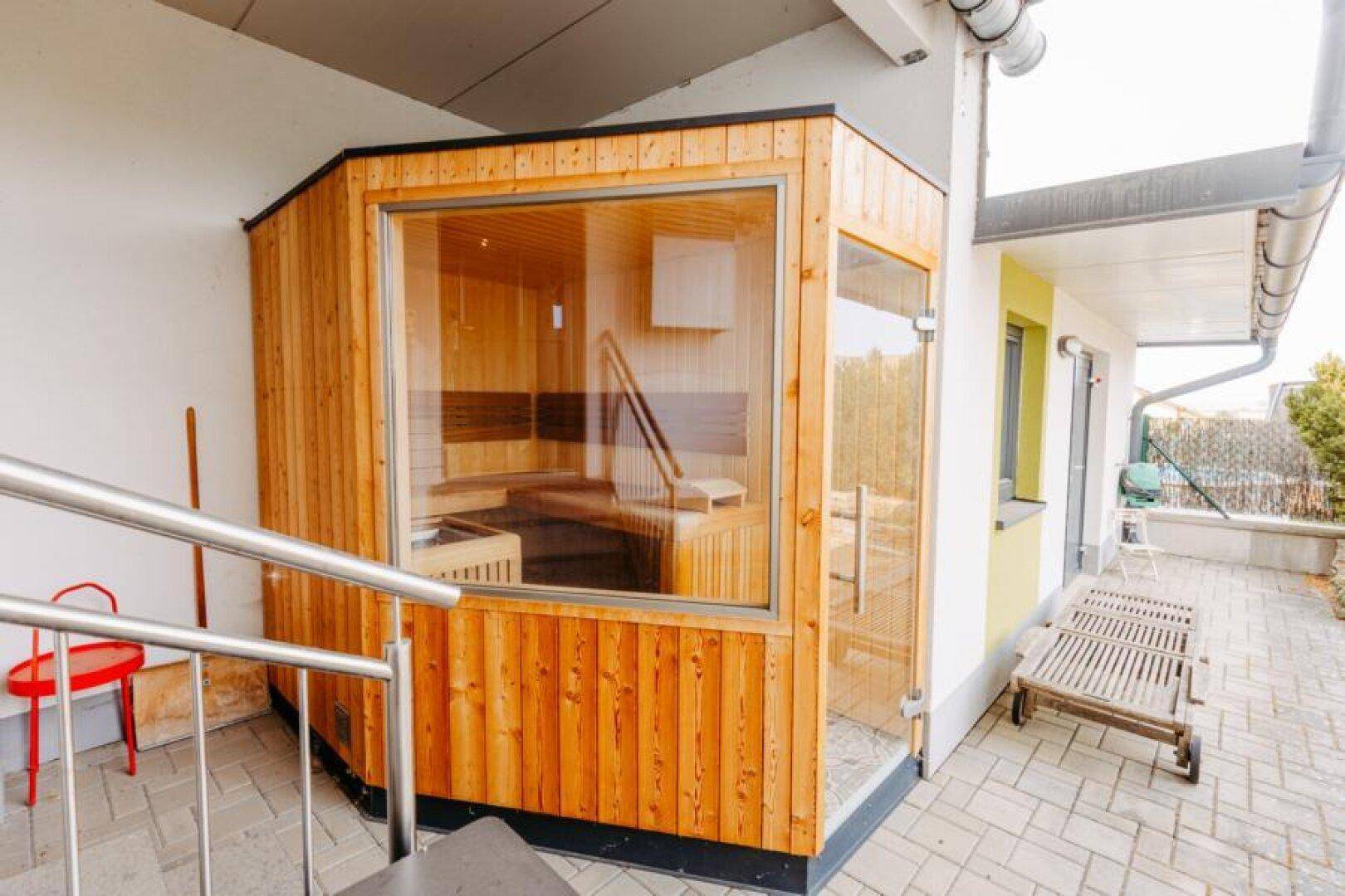Moderne Außensauna mit Holzverkleidung und großem Fenster, ein Highlight im Außenbereich.