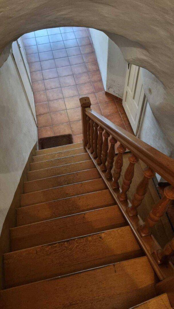 Holztreppe führt hinunter in einen gefliesten Flur, der zu weiteren Räumen führt.