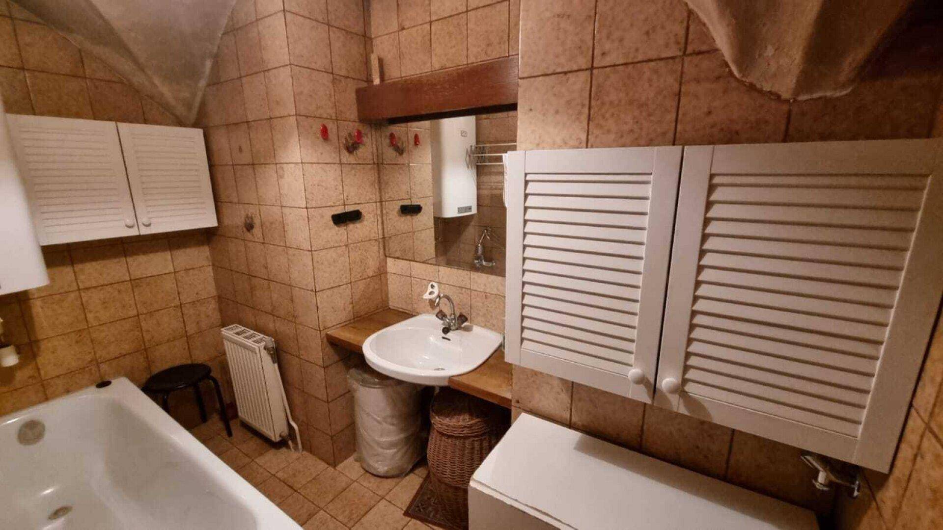 Rustikales Badezimmer mit braunen Fliesen, Badewanne und einem Waschbecken mit Holzablage.