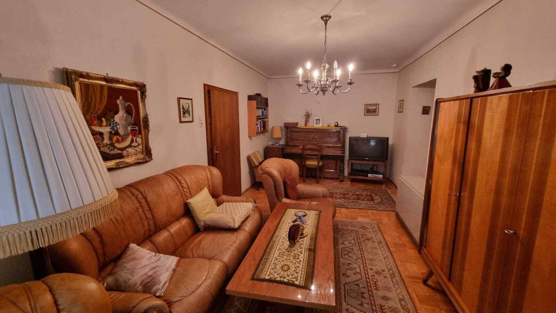 Wohnzimmer mit Ledersofa, Couchtisch, Teppich und einem Klavier im Hintergrund.