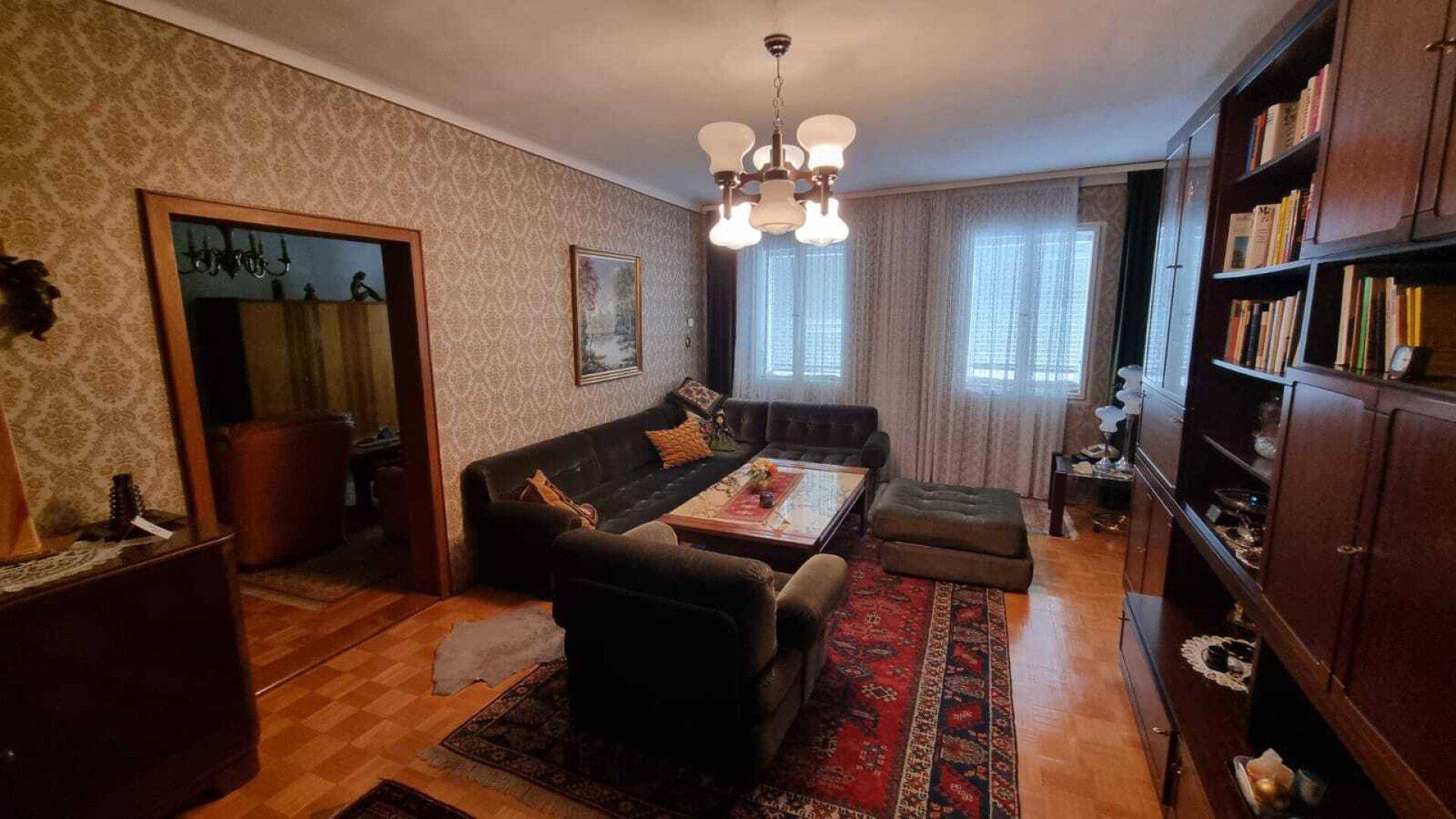 Gemütliches Wohnzimmer mit gemusterter Tapete, Sofa, Sessel und einem Teppich auf Parkettboden.