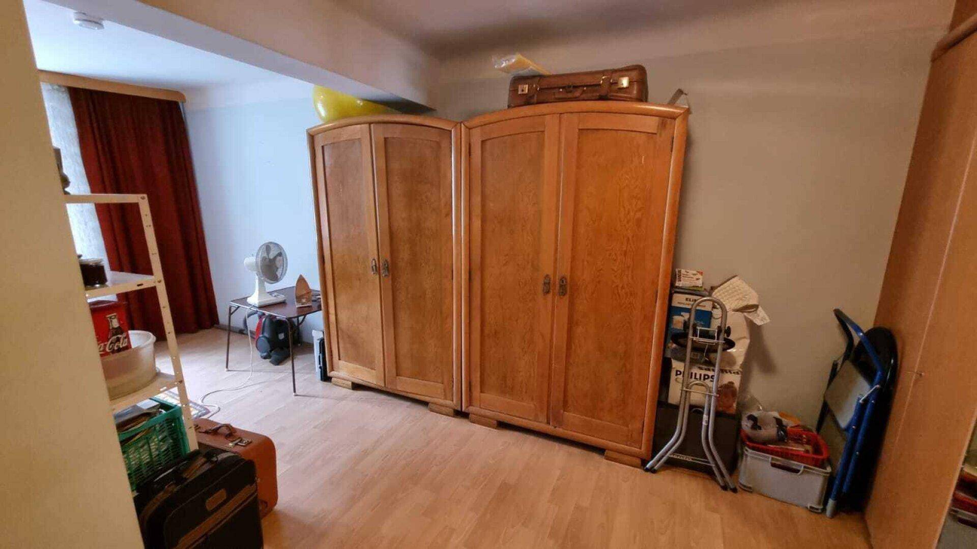 Schlafzimmer mit Holzschränken, Parkettboden und verschiedenen Gegenständen, die auf Lagerung hindeuten.