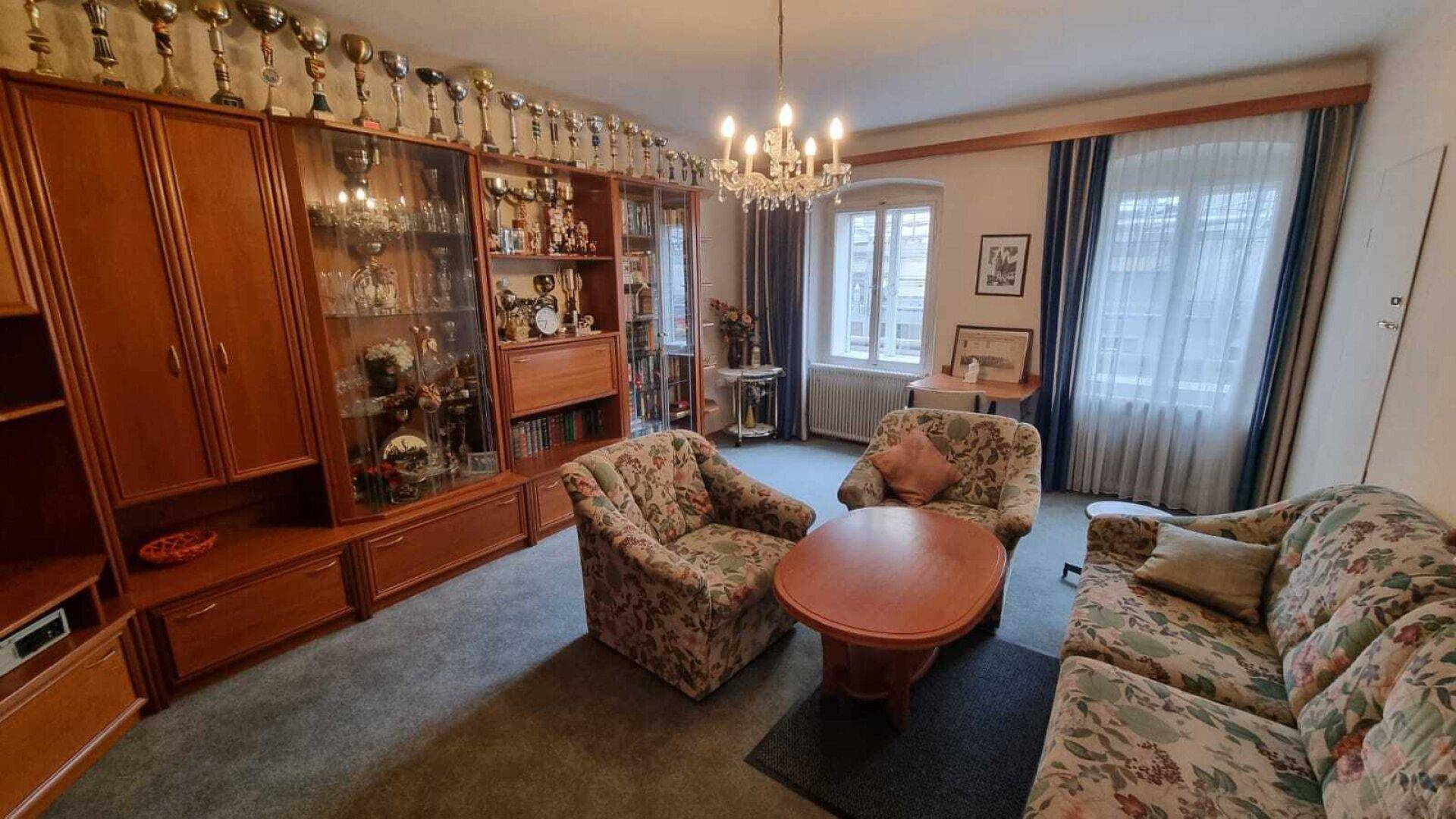 Geräumiges Wohnzimmer mit Teppichboden, einer großen Schrankwand und traditionellen Möbeln.