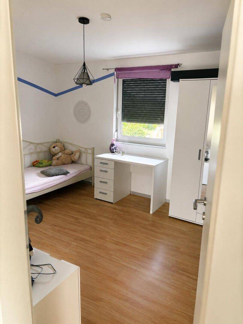 Helles Schlafzimmer mit Einzelbett, Schreibtisch und weißem Kleiderschrank.