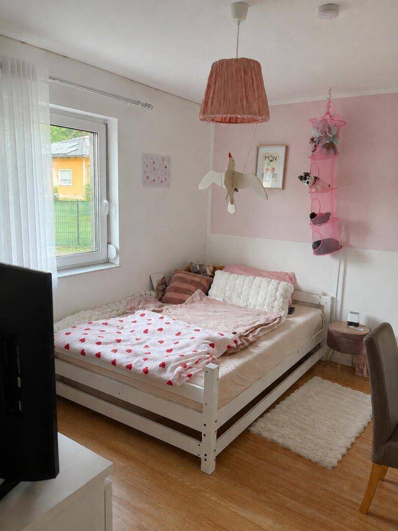 Kinderzimmer mit Einzelbett, rosa Wandakzenten und hellem Holzboden.