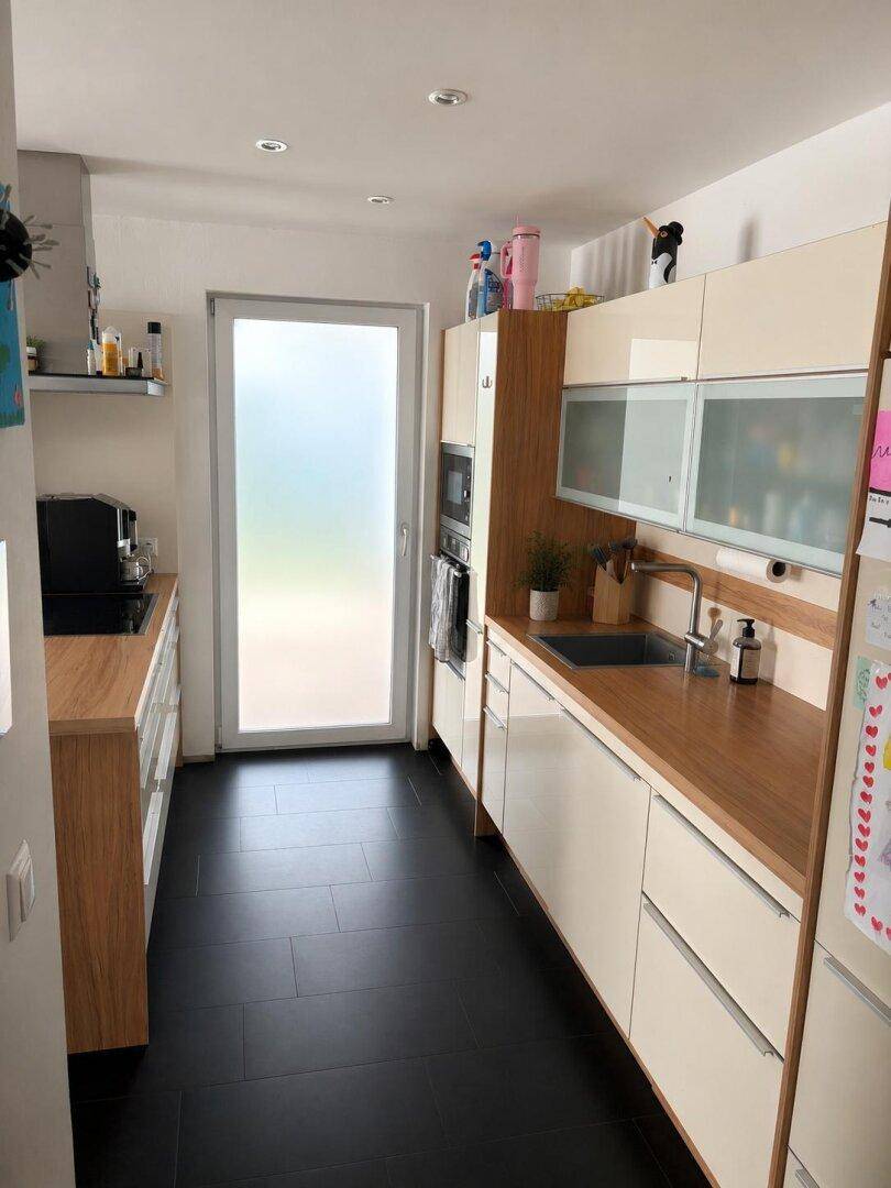 Moderne Küche mit hellen Schränken, Holzarbeitsplatten und dunklen Fliesenböden.