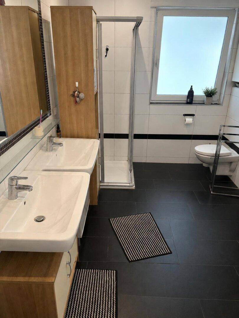Modernes Badezimmer mit Doppelwaschbecken, Duschkabine und Fenster.
