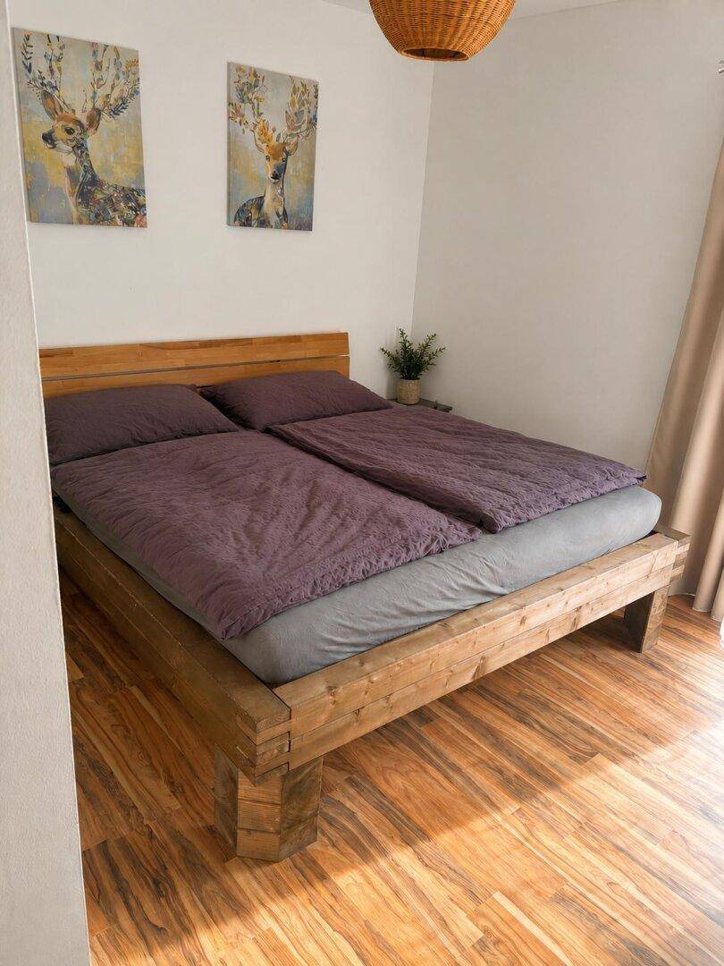 Schlafzimmer mit Holzbettgestell, Holzboden und schlichter, moderner Einrichtung.