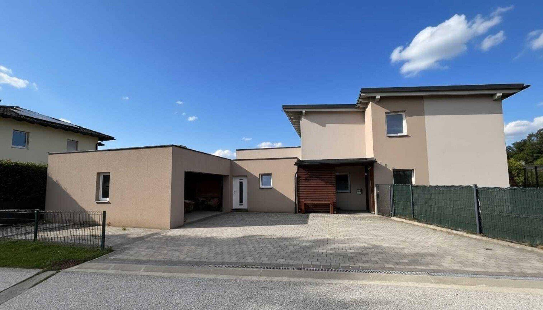 Ansicht des modernen Einfamilienhauses mit integrierter Garage und breiter gepflasterter Zufahrt.