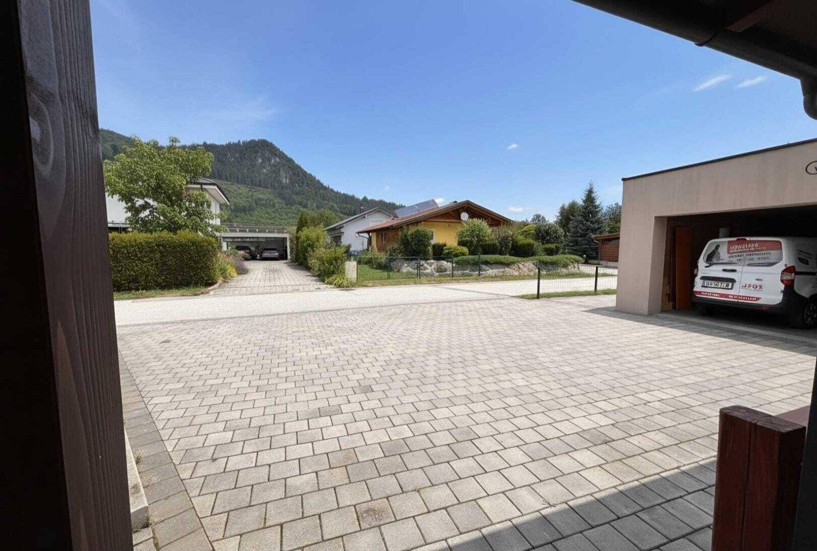 Gepflasterte Einfahrt mit Blick auf die umliegende Wohnsiedlung und bewaldete Berge im Hintergrund.