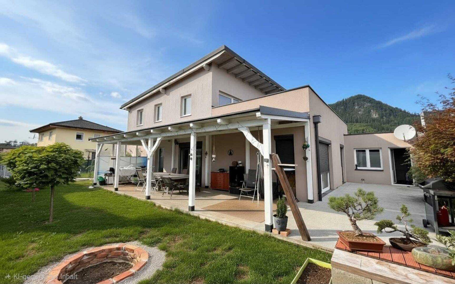 Überdachte Terrasse mit Gartenmöbeln und Rasenfläche, umgeben von grüner Landschaft und Bergen.