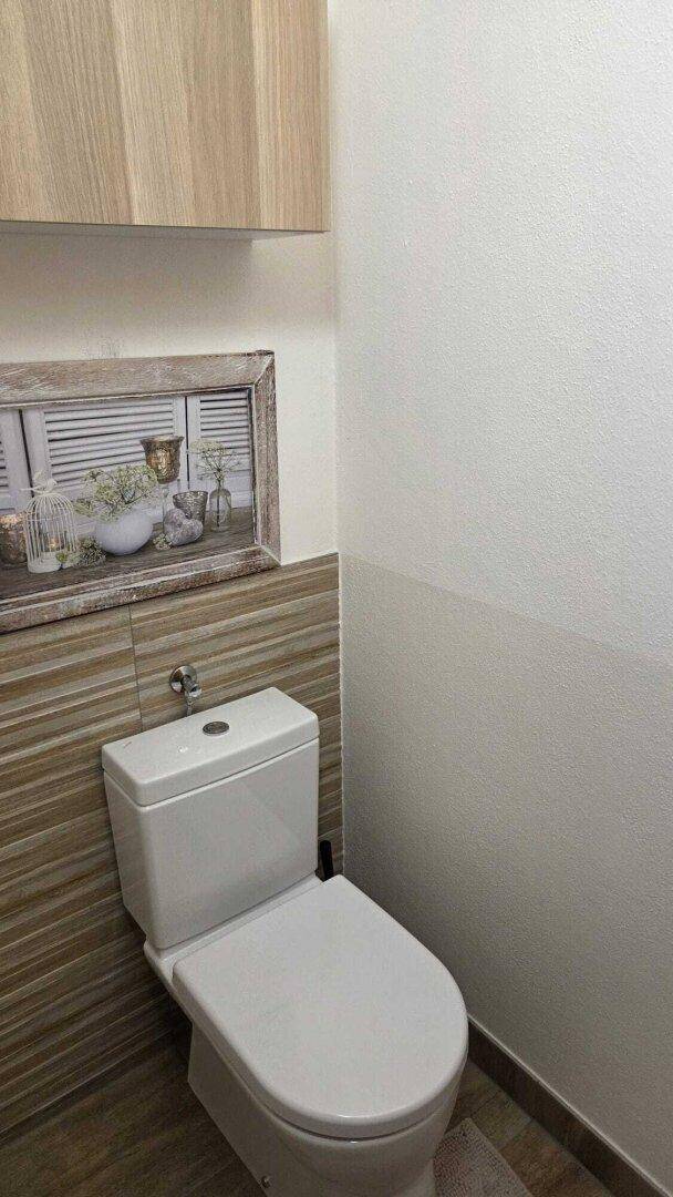 Separate Toilette mit Wand-WC und teilweise gefliesten Wänden in neutralen Farbtönen.