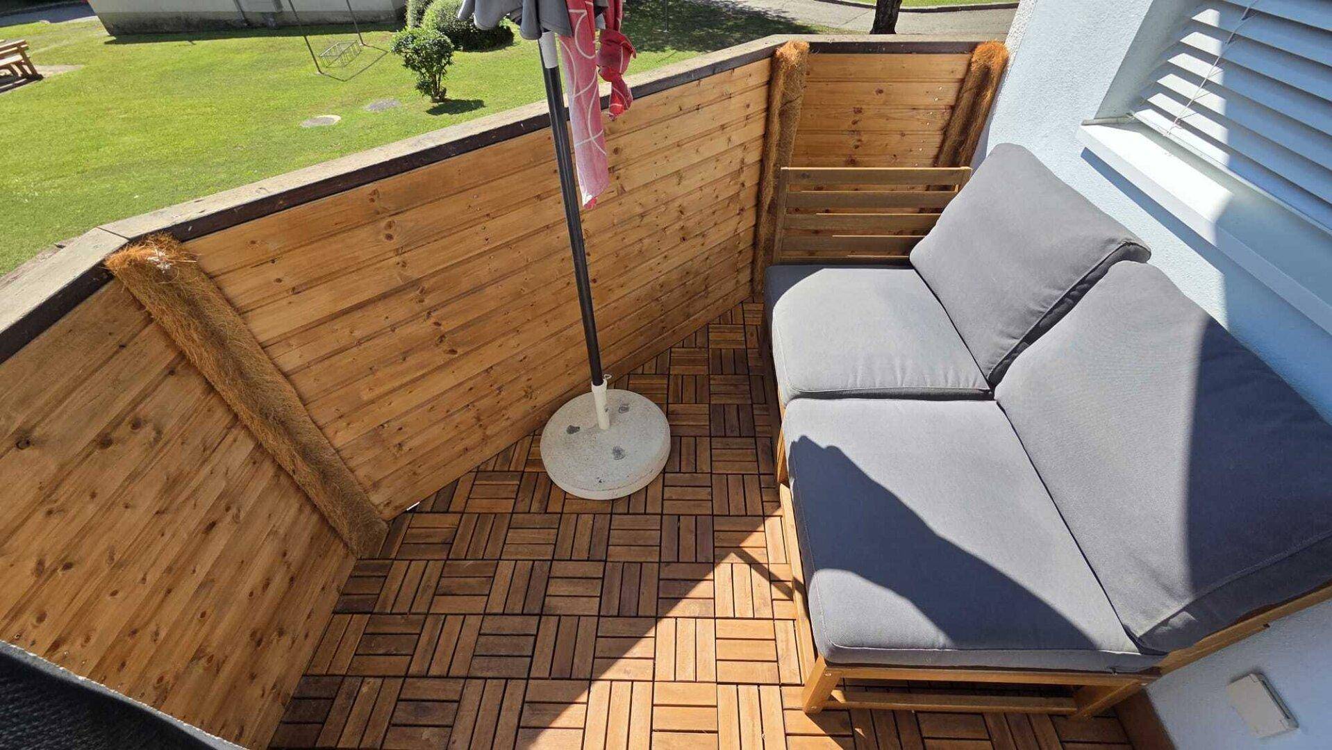 Gemütlicher Balkon mit Holzbodenfliesen und einer Sitzgelegenheit, ideal zum Entspannen im Freien.