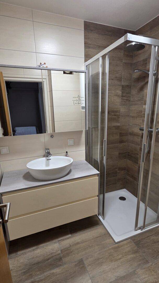 Modernes Badezimmer mit Duschkabine, Einzelwaschbecken und hellen Fliesen an Wänden und Boden.