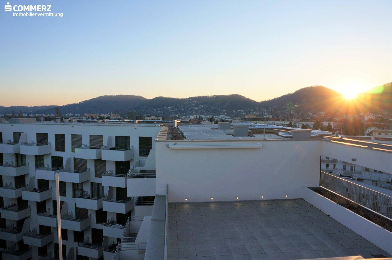 Geräumige Dachterrasse mit Fliesenboden und weitem Blick auf die umliegenden Berge bei Sonnenuntergang.