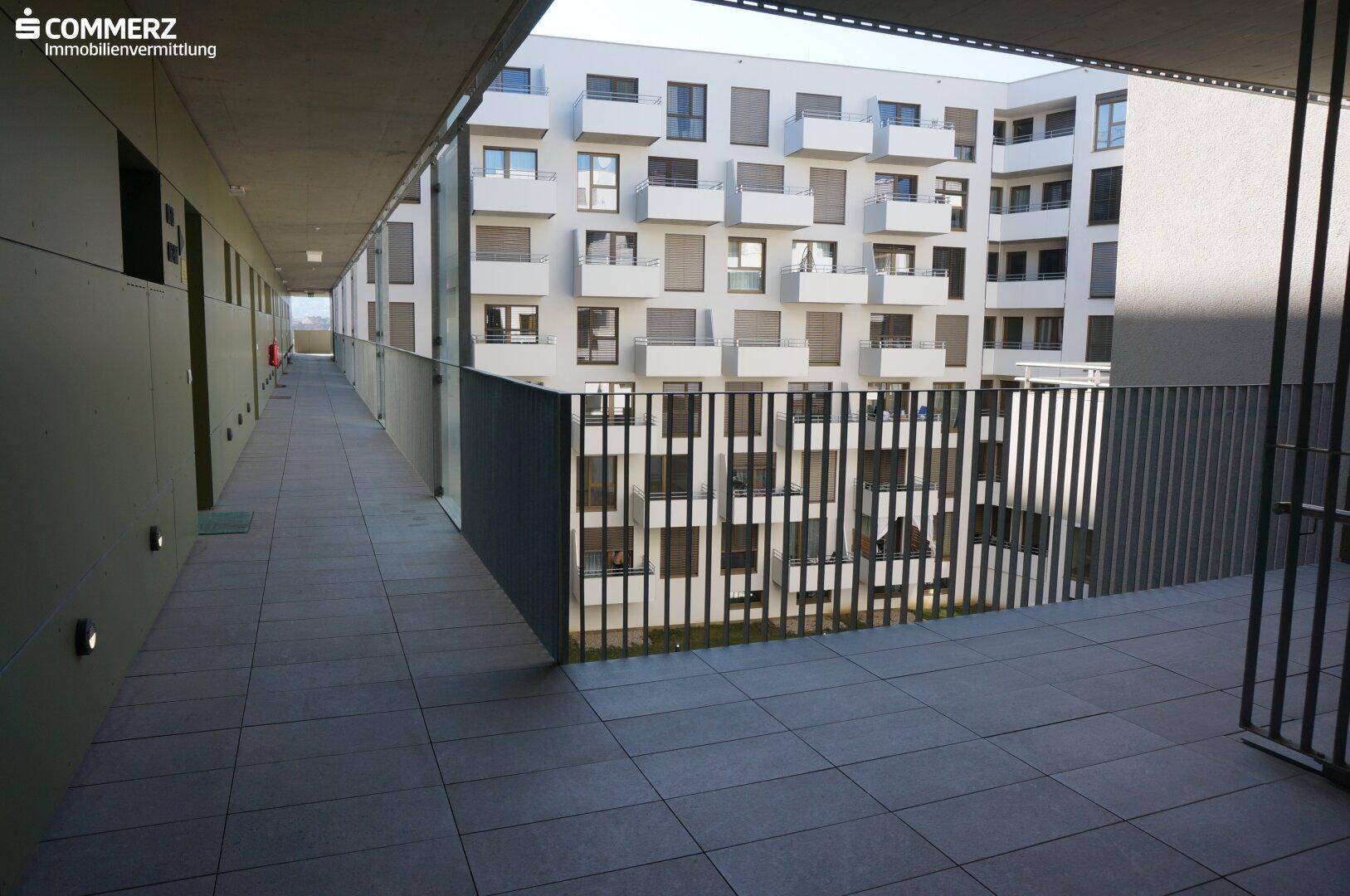 Langer, gefliester Flur im Obergeschoss mit Blick auf den Innenhof der Wohnanlage.