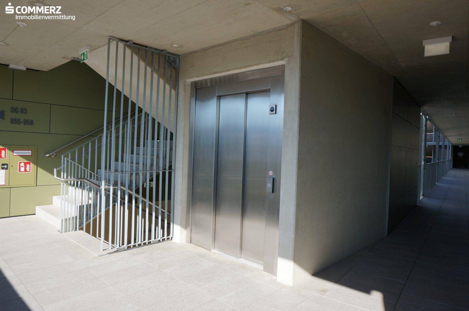 Moderner Aufzug und Treppenhaus in einem hellen Gemeinschaftsbereich des Wohngebäudes.