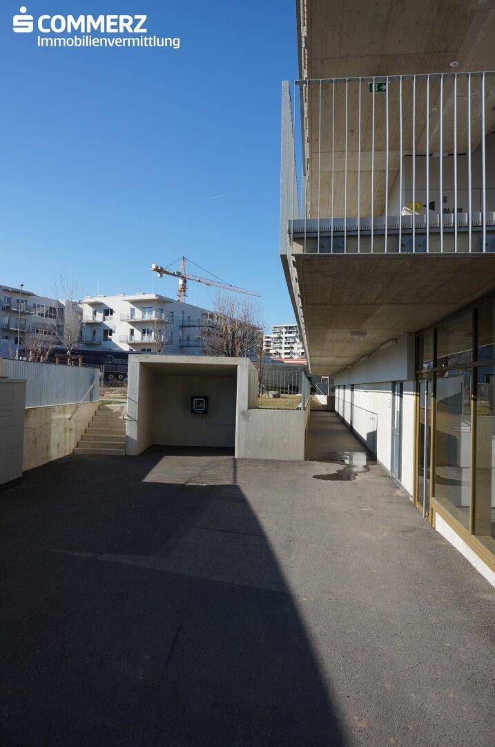 Außenansicht des Erdgeschosses mit Zufahrt zur Tiefgarage und einem Baukran im Hintergrund.
