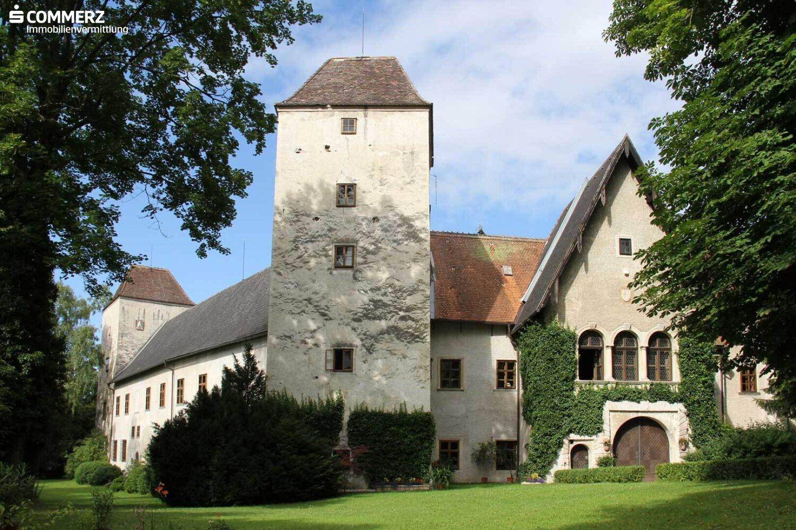 Historisches Anwesen mit imposantem Turm und üppiger Begrünung, umgeben von altem Baumbestand.