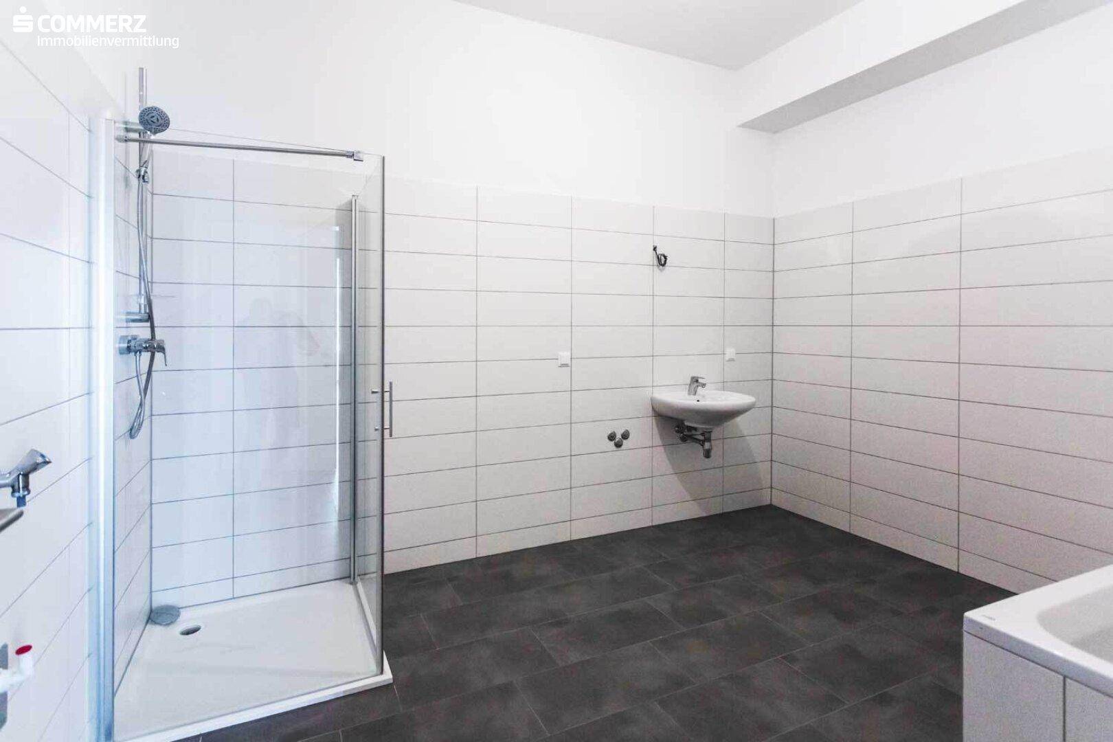 Modernes Badezimmer mit weißen Wandfliesen, dunklem Boden und einer geräumigen Duschkabine.