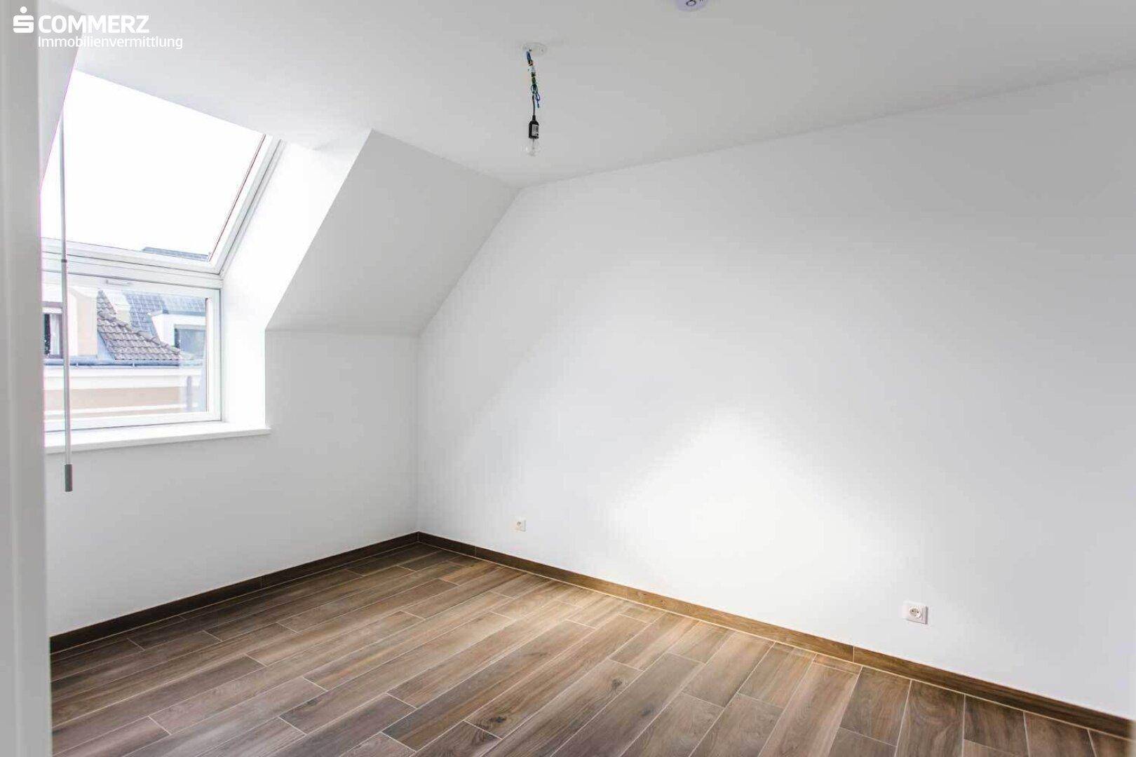 Kleiner Dachbodenraum mit Laminatboden, schrägen Wänden und einem Dachfenster für Tageslicht.