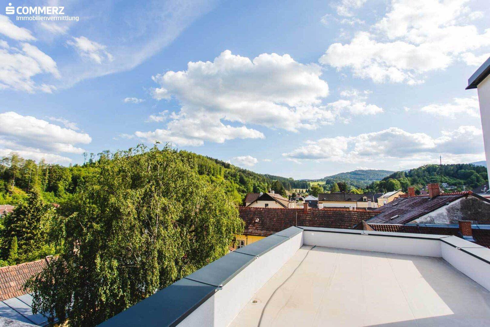 Unmöblierte Dachterrasse mit weitem Blick auf grüne Hügel und die umliegende Landschaft.
